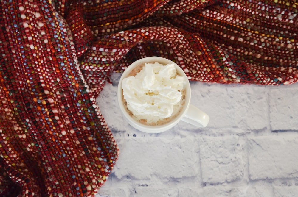 white ceramic mug near red textile