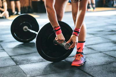 Close-up of hands adjusting weights on a barbell with orange and black gym colors.