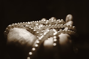 A hand gently holding a string of pearls, highlighted by soft lighting that creates a serene and elegant atmosphere. The pearls are prominently displayed, showcasing their smooth texture and spherical shape, while the background remains dark and blurred.