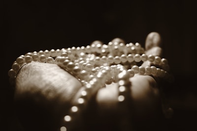 A hand gently holding a string of pearls, highlighted by soft lighting that creates a serene and elegant atmosphere. The pearls are prominently displayed, showcasing their smooth texture and spherical shape, while the background remains dark and blurred.