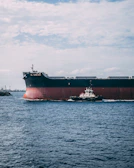 A sturdy tug boat maneuvering a large cargo ship under a clear blue sky.