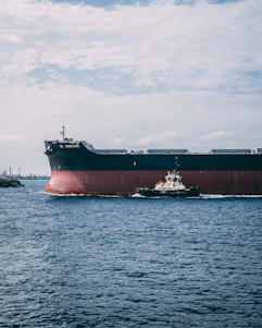 A tugboat assisting a large cargo ship near the London Medway port under a clear sky.