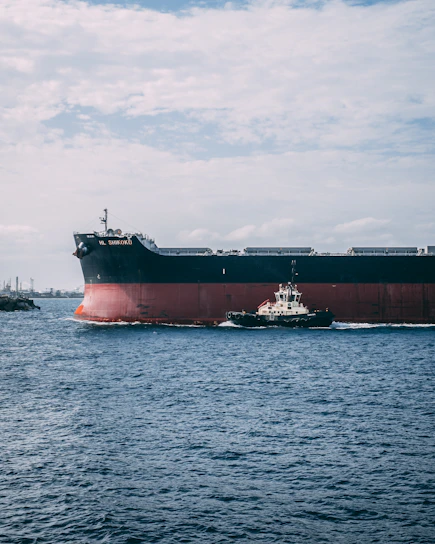 A tugboat assisting a large cargo ship near the London Medway port under a clear sky.