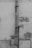 An old, weathered downpipe attached to a wall, which has patches of peeling paint and discoloration. The wall features a rough, textured surface with noticeable wear and tear. There is a smaller black cable running parallel to the downpipe, secured at various points.