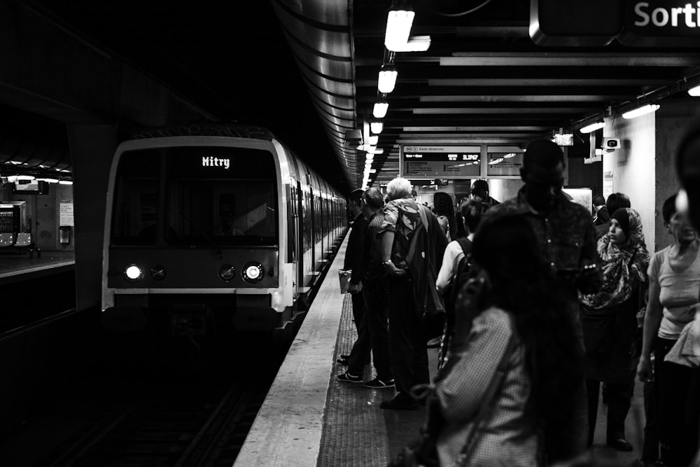 Grupo de personas esperando el tren en fotografía en escala de grises