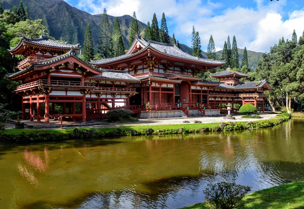 red and white temple near body of water and mountain under cloudy sky