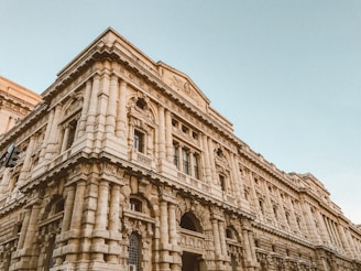 A grand, historic stone building with intricate architectural details, including carved columns and ornamental friezes. The structure has multiple arched windows and a prominent facade, showcasing classical design elements.