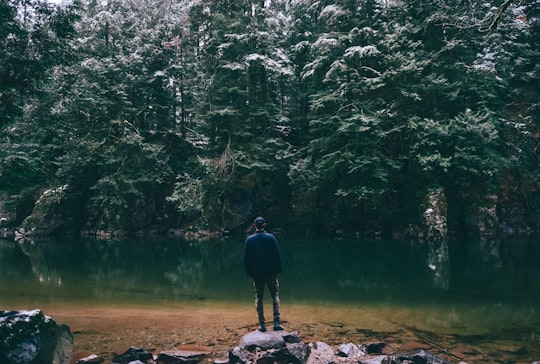 man standing on rock facing body of water surrounded with trees in North Vancouver Canada