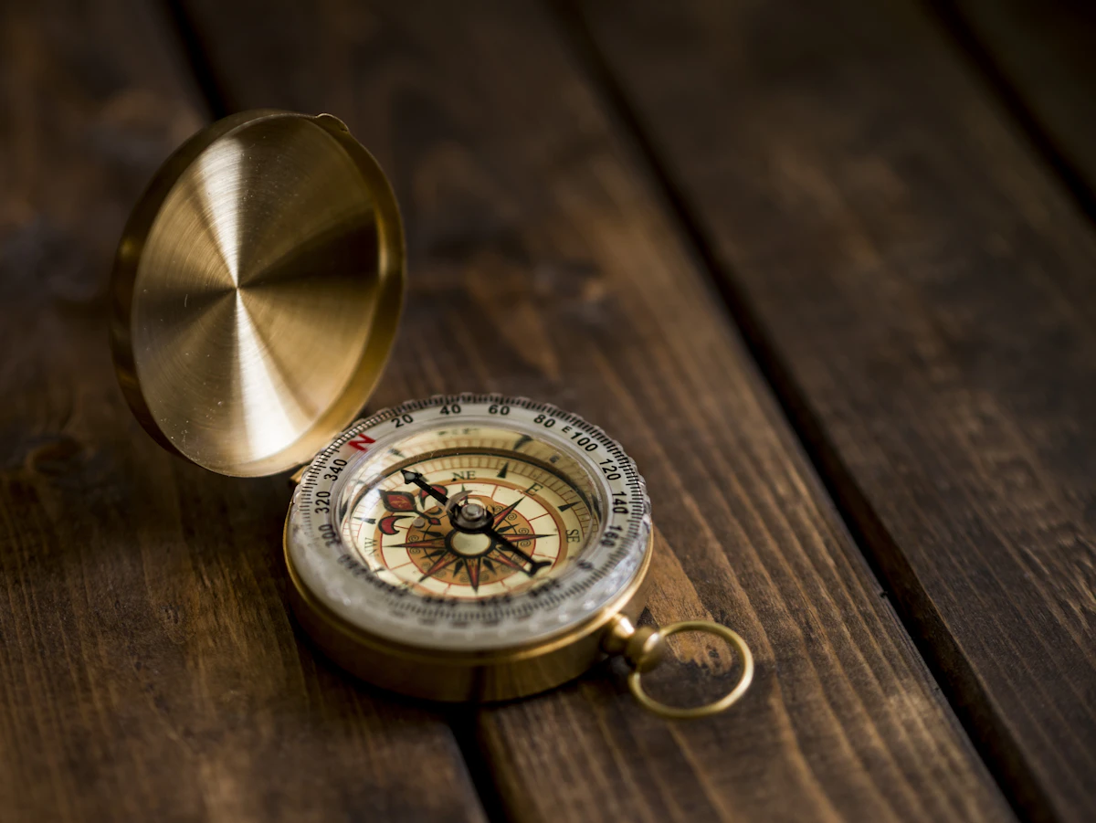 A vintage brass compass resting on a wooden desk