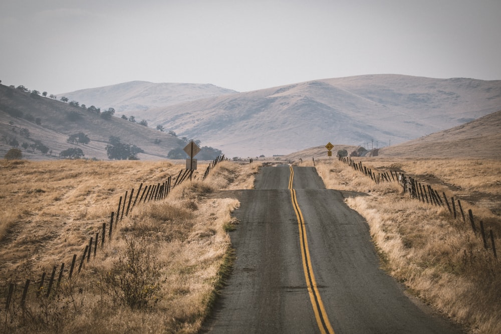 gray concrete road between brown grass field