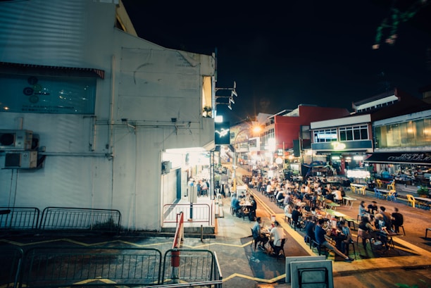 A lively urban street food scene with people enjoying meals at outdoor tables under string lights.