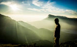 A golden sunrise casting light over the Himalayas with a lone traveler meditating on a rocky ledge.