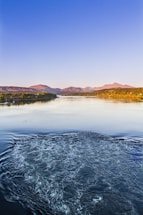 A gentle sky blue river winding toward the viewer with misty gray mountains and a bright yellow sun rising behind them.