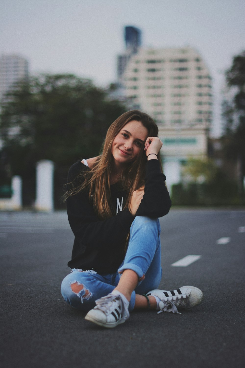 mulher sorrindo enquanto está sentada na estrada com a mão apoiada em cima do joelho