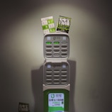 A charging station with multiple slots for charging devices, featuring two advertising flyers attached to the top. The station displays a logo and has various buttons and indicators.