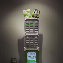 A charging station with multiple slots for charging devices, featuring two advertising flyers attached to the top. The station displays a logo and has various buttons and indicators.