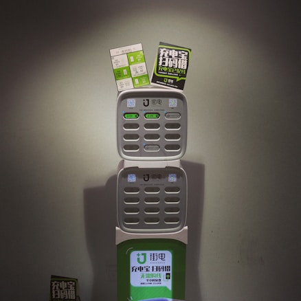 A charging station with multiple slots for charging devices, featuring two advertising flyers attached to the top. The station displays a logo and has various buttons and indicators.