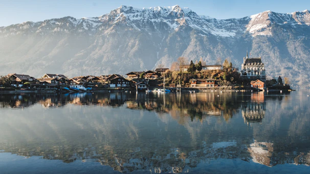 A serene lakeside village nestled among lush green mountains at golden hour.