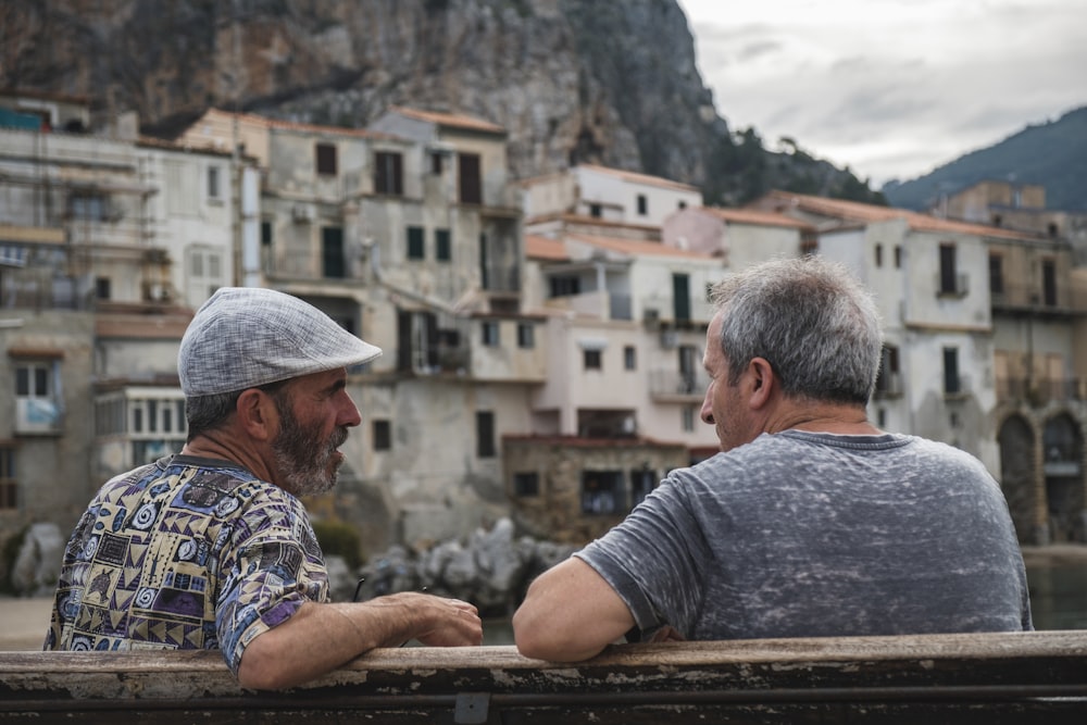 two men sitting on bench talking near village during day