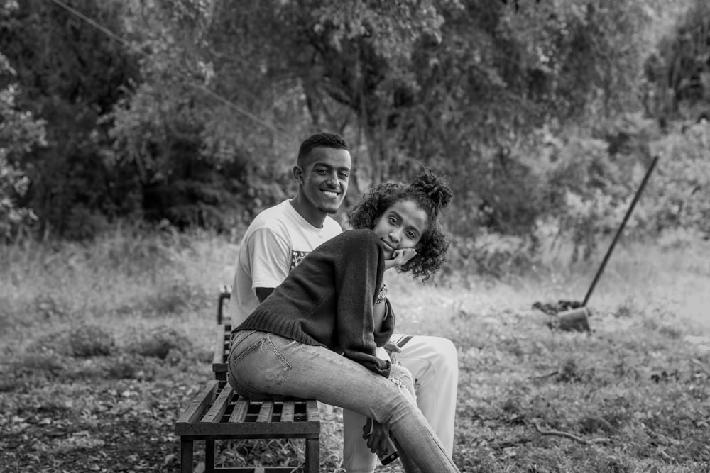 Graustufenfoto einer Frau und eines Mannes, die auf einer Bank in der Nähe von Bäumen sitzen