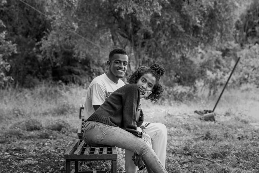 grayscale photo of woman and man sitting on bench near trees