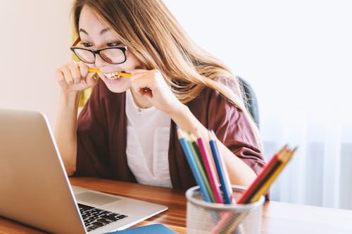 Femme mordant son crayon en regardant l'écran de son ordinateur, comme si elle se demandait quoi poster sur son site Instagram Story.