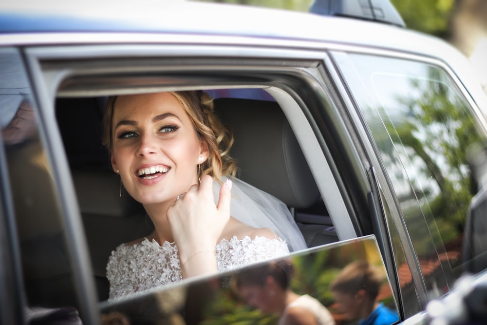 woman wearing wedding dress smiling inside car