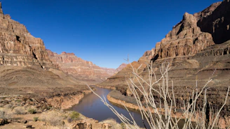 Wide shot of the canyon landscape with the river winding through and distant mountains under a clear sky.