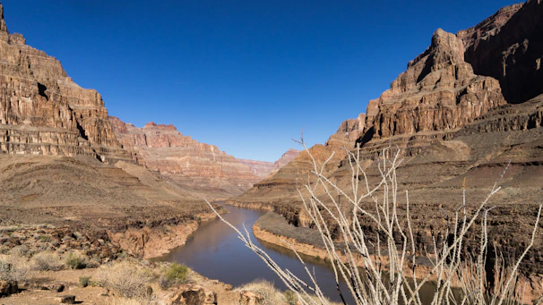 Wide shot of the canyon landscape with the river winding through and distant mountains under a clear sky.