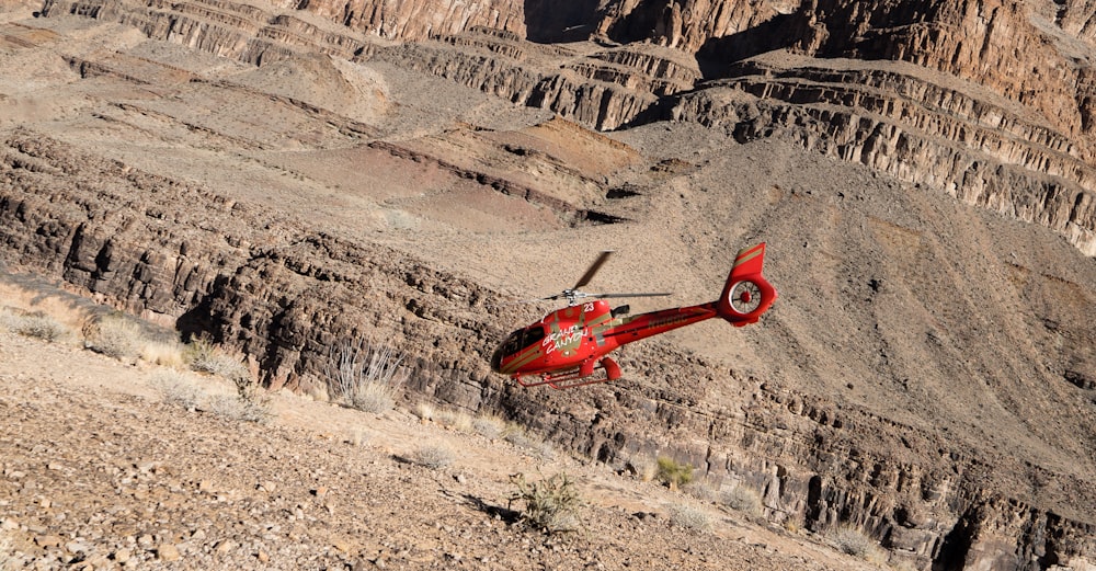 red R/C helicopter flying over gray sand
