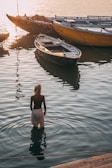 man wearing white bottoms in water near brown wooden canoe