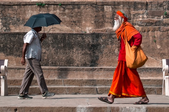man walking beside man holding umbrella in Varanasi India