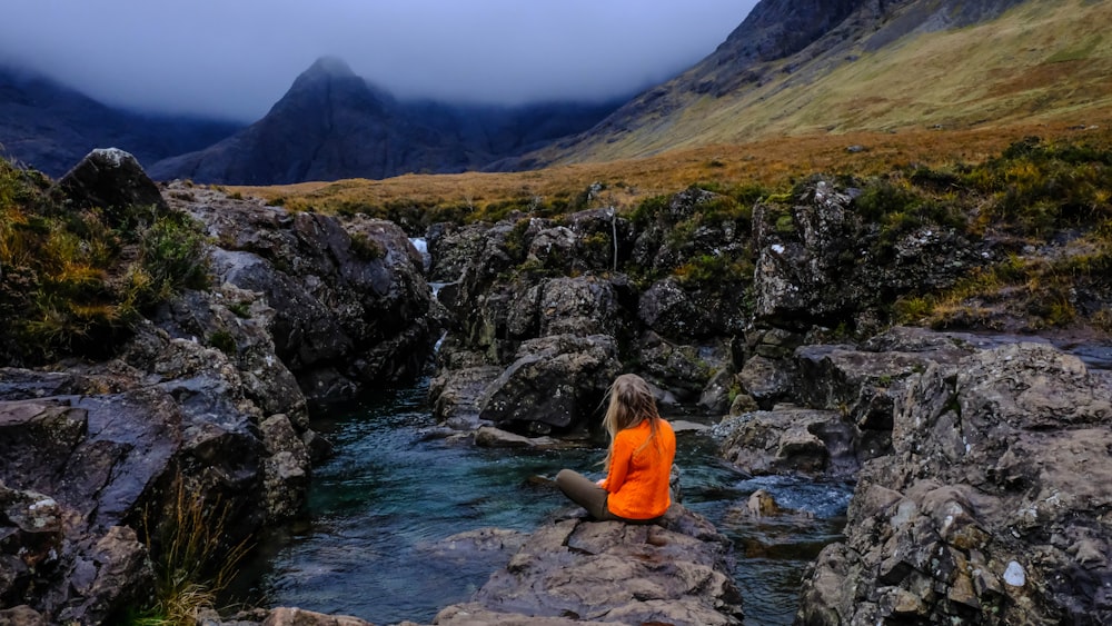 Frau sitzt auf einem Felsen, umgeben von Wasser