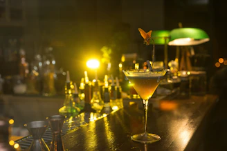 Close-up of a beautifully garnished cocktail on a wooden bar counter with soft lighting.