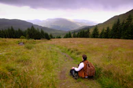 A backpacker pausing on a trail overlooking a vast forest valley.