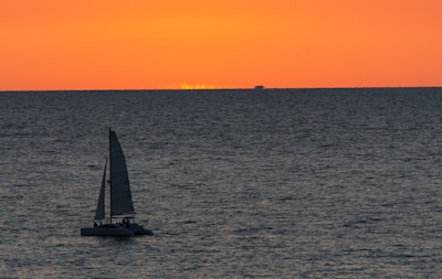 A sailboat gently gliding across calm waters under a vibrant orange and pink sunset.
