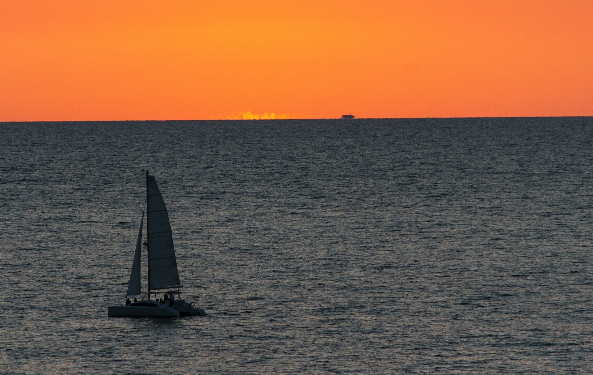 A serene sailboat gliding gently across calm waters under a vibrant orange and pink sunset sky.