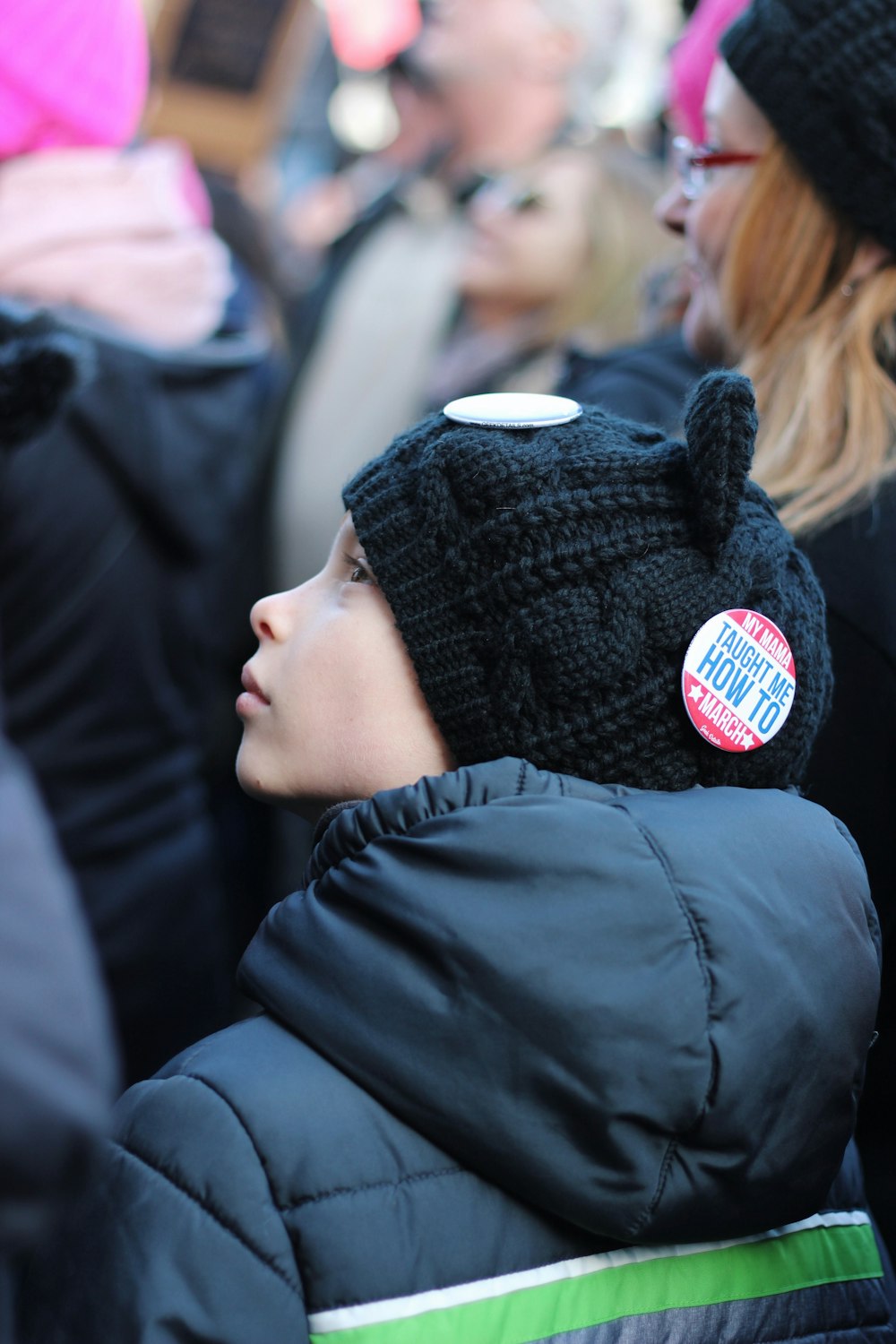close up photo of boy's back sitting looking to the left wearing knit cap and hooded jacket