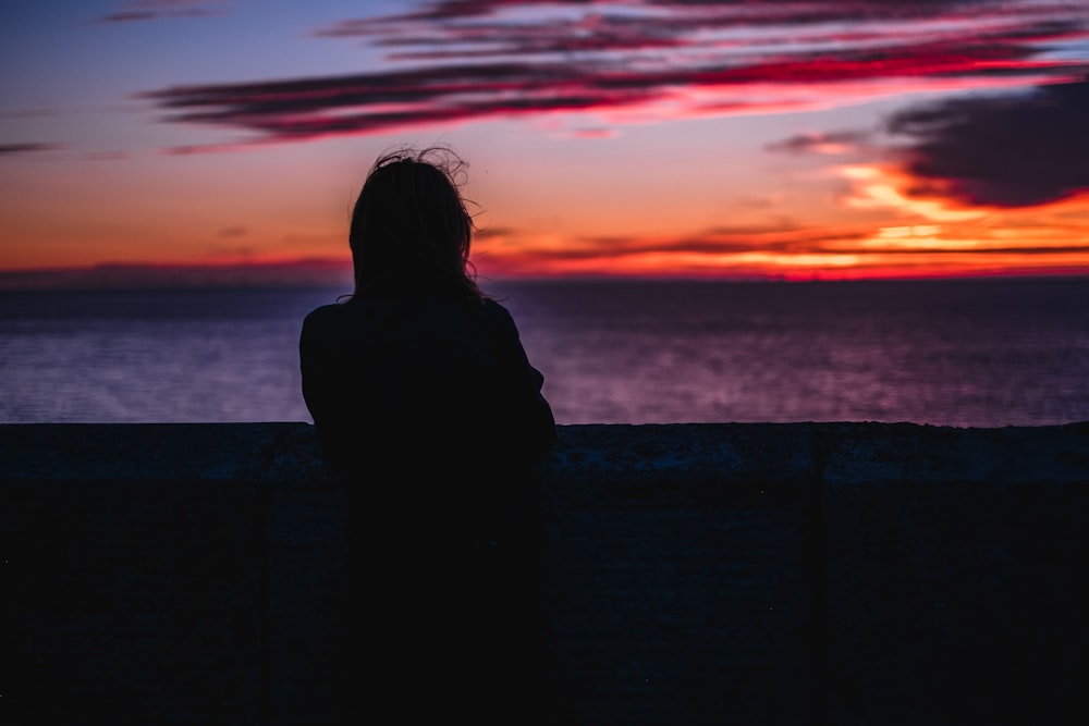 ゴールデンアワーに海を眺めながら立っている人のシルエット写真