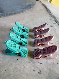 A series of plastic clips are arranged in two parallel lines on a rough concrete surface. The clips on the left are green, while those on the right are brown. The surface on which they rest has visible texture and slight discoloration.