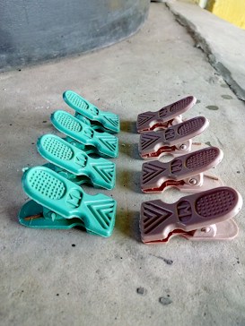 A series of plastic clips are arranged in two parallel lines on a rough concrete surface. The clips on the left are green, while those on the right are brown. The surface on which they rest has visible texture and slight discoloration.