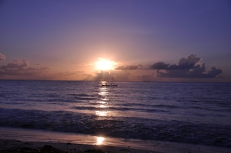 A serene coastal horizon at sunset with gentle waves and a small sailboat in the distance.