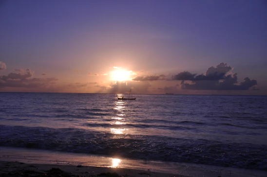 A serene ocean sunset with a small boat gently sailing, evoking calm and adventure.