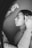 A person is adjusting their hair while looking into a mirror. The image is in black and white, focusing on the side profile of the person. The subject is wearing a long-sleeved garment and appears concentrated on their reflection.