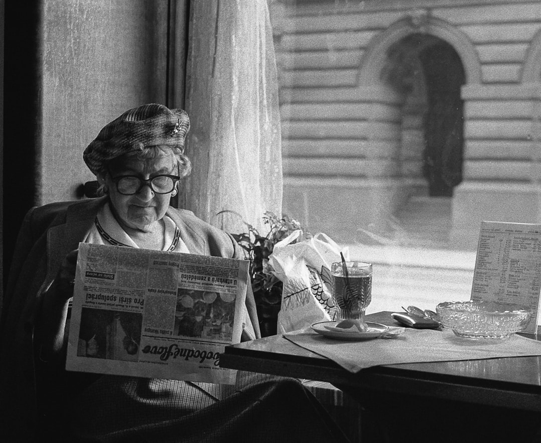grayscale photo of woman sitting while reading newspaper