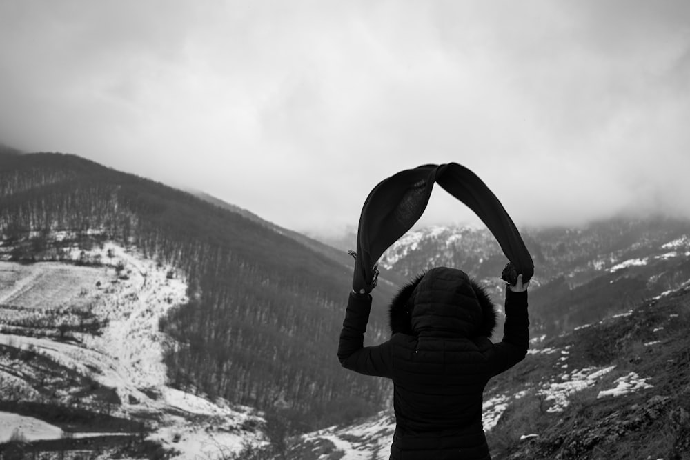 person wearing hooded jacket standing while looking at the snow-covered mountain during daytime