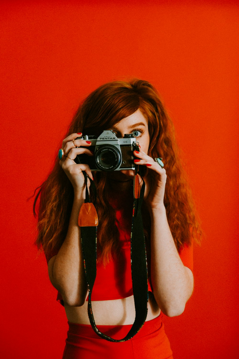 mujer en la parte superior y la parte inferior roja sosteniendo la cámara Pentax