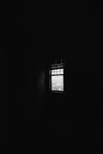 A dimly lit room with faint outlines of shackles and a single beam of light breaking through a small window.