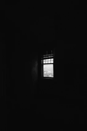 A dimly lit room with faint outlines of shackles and a single beam of light breaking through a small window.