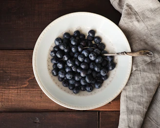 A close-up of a hand-thrown, bright yellow stoneware bowl filled with fresh berries on a rustic wooden table.